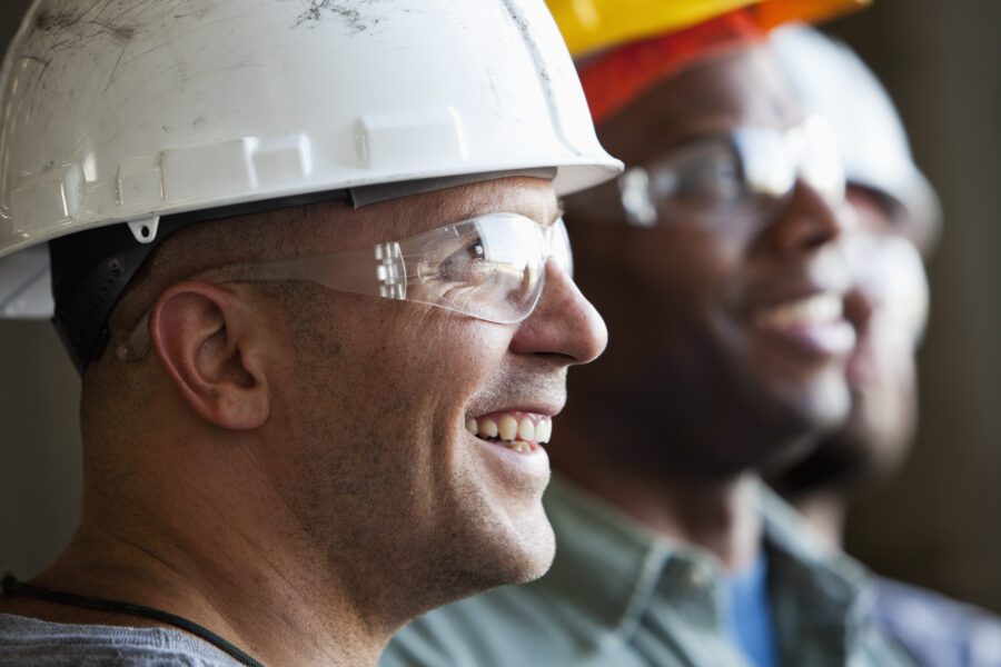 Men smiling in construction hats and glasses close up