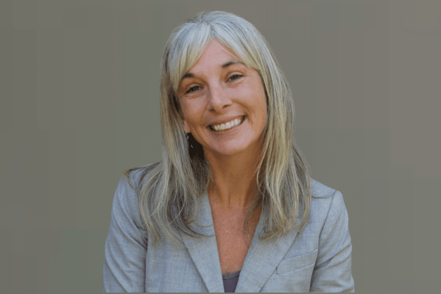 Woman headshot smiling gray/green background gray blazer